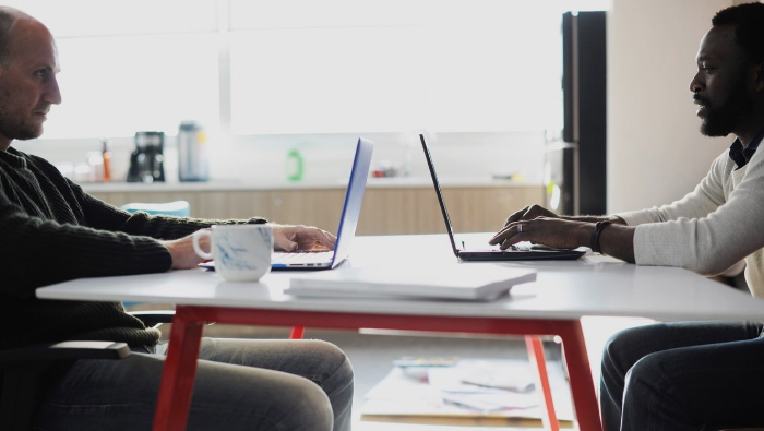 two people are sitting with laptops at a table opposite each other